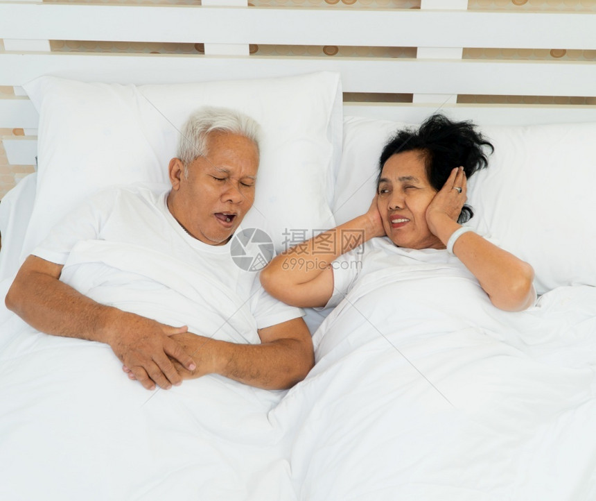 不眠休成熟失亚裔老妇人张开双眼用手遮耳盖朵躺在她丈夫旁边的床上丈夫打呼噜制造噪音婚姻问题图片