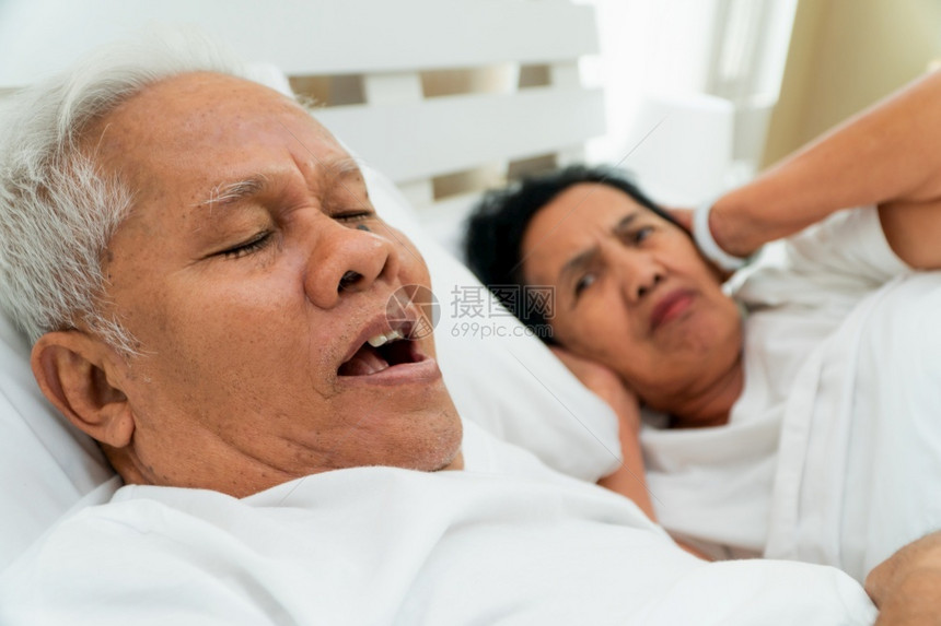 枕头男亚裔老妇人张开双眼用手遮耳盖朵躺在她丈夫旁边的床上丈夫打呼噜制造噪音婚姻问题成熟图片