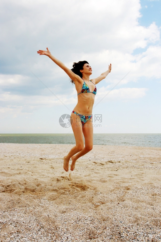 旅行户外海洋女孩在滩上跳跃面和阴云的天空背景图片