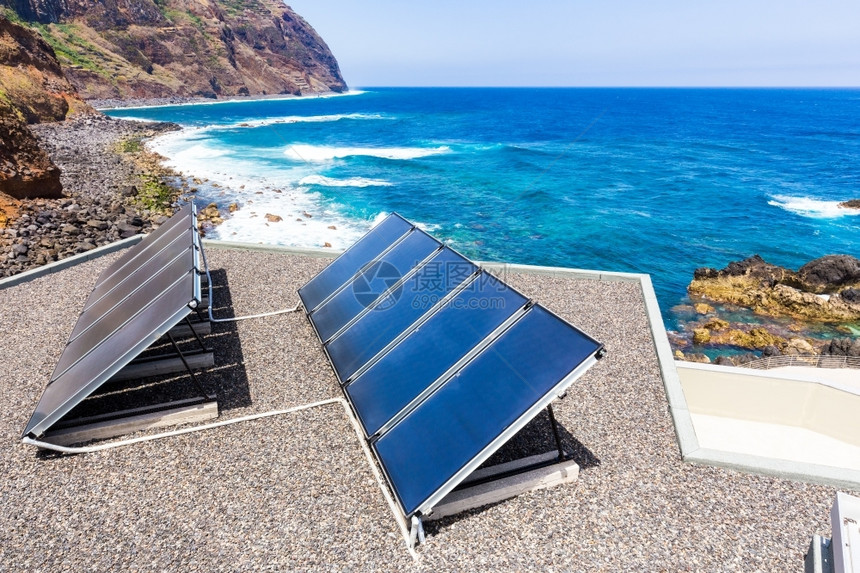 海滩洋和山丘附近房屋上的蓝色太阳能电池板面产生地中海图片