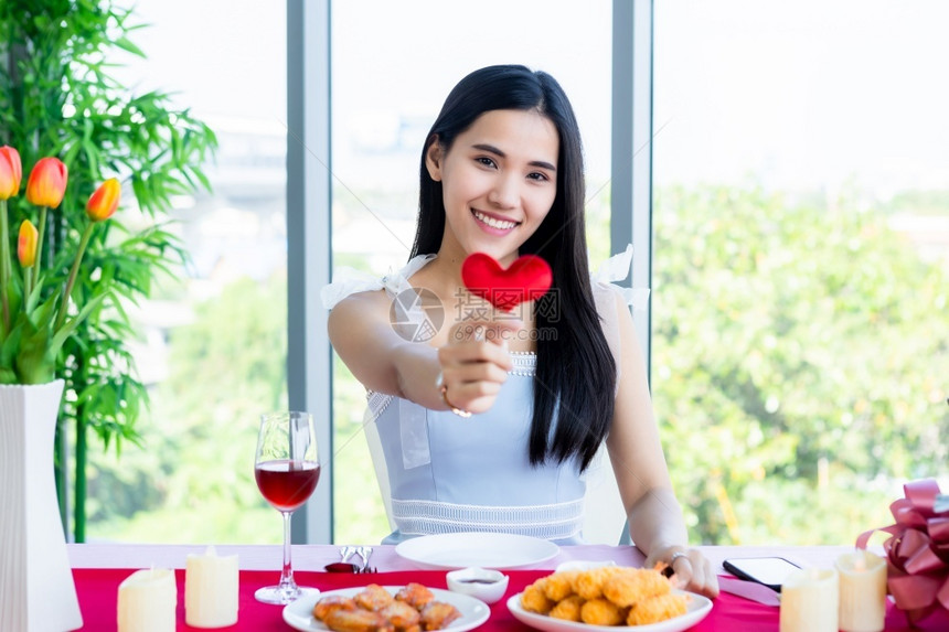 快乐的美丽情人节概念笑的亚洲快乐年轻女坐在餐桌食物展上抱着小红心在餐厅背景中形成笑声在餐馆背景中假期图片