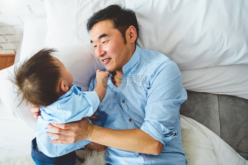 可爱的男生清白亚洲父亲和儿子早上一起在卧室的白床上玩两个人在家里有闲暇时间在家中享受休闲时间的人生活方式概念笑声图片