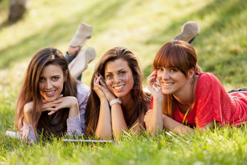 三个女孩趴在草地上愉快地看着平板图片