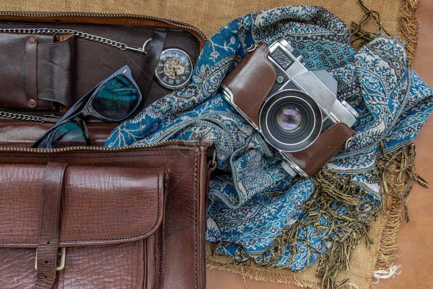 放松时尚古老的摄影相机和棕色皮包上面有围巾眼镜和袋布背景口手表的棕色皮假日旅行概念设计颜色图片