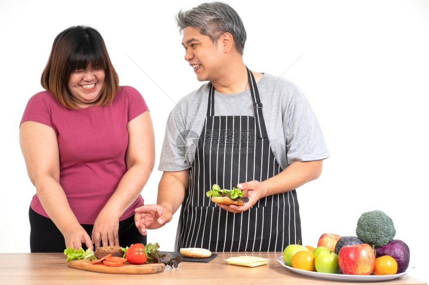 烹饪快乐的超重夫妇在厨房做汉堡餐室吃一个汉堡A蔬菜放在桌子上幸福的家庭和狂欢饮食的概念愉快男朋友图片