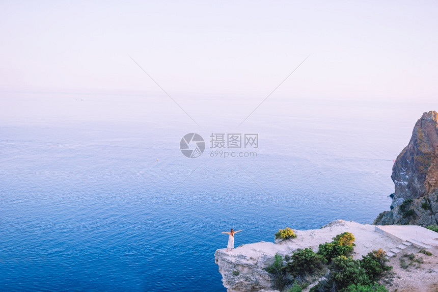 穿着白裙子的快乐女孩在山度假悬崖海岸边缘露天旅游女客探索高的人们图片