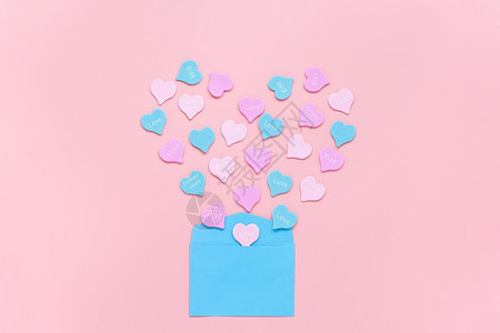 象征带有文字LOVEKISSFOREVERYOURS的彩色心以形式从粉红色背景的蓝纸信封中飞出情人节概念爱表白的礼物复制空间带有背景图片