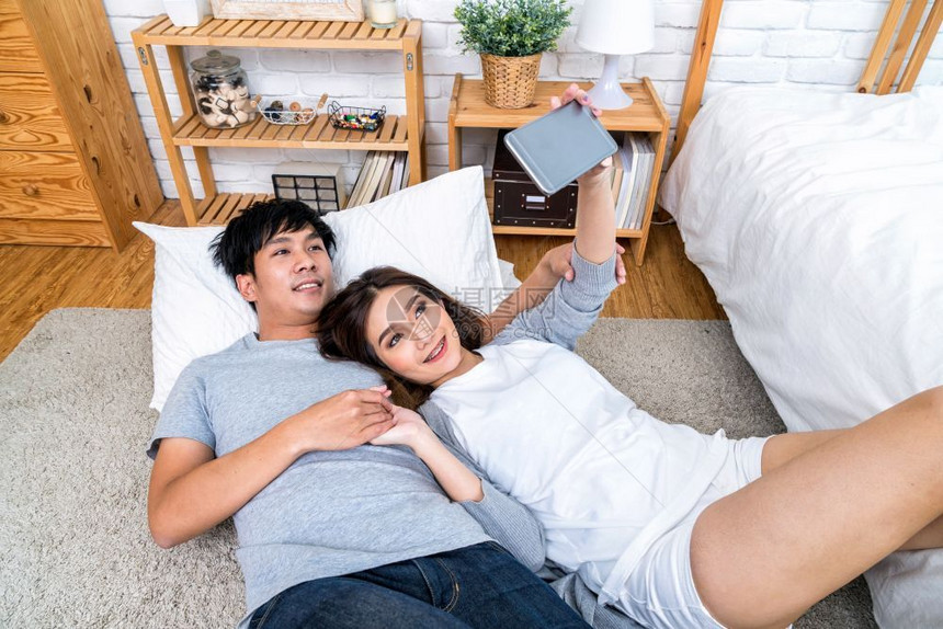 亚洲快乐情人的顶端视野使用技术智能电话在地板上自拍用毯在卧室里家情侣自拍概念日本人最佳浪漫图片