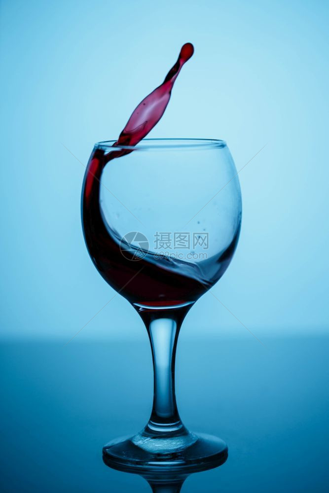 蓝色背景的黑光彩玻璃上杯子中的红葡萄酒喷洒杯果汁漩涡图片