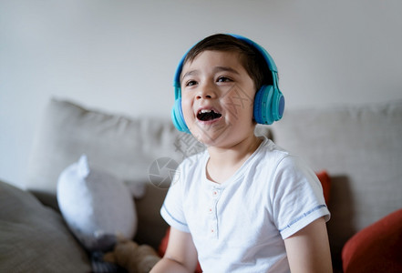 声音随意的亚洲人快乐孩子穿着耳机仰望微笑的脸快乐男孩听音坐在沙发上玩电子游戏或在家客厅休息时的可爱基德CuteKid坐在沙发上音乐高清图片素材
