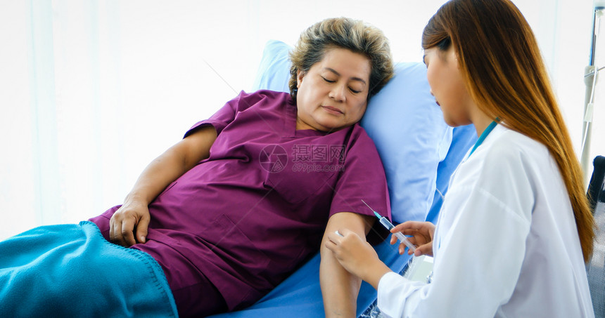 医生用注射器给躺在床上的生病老妇人注射疫苗图片