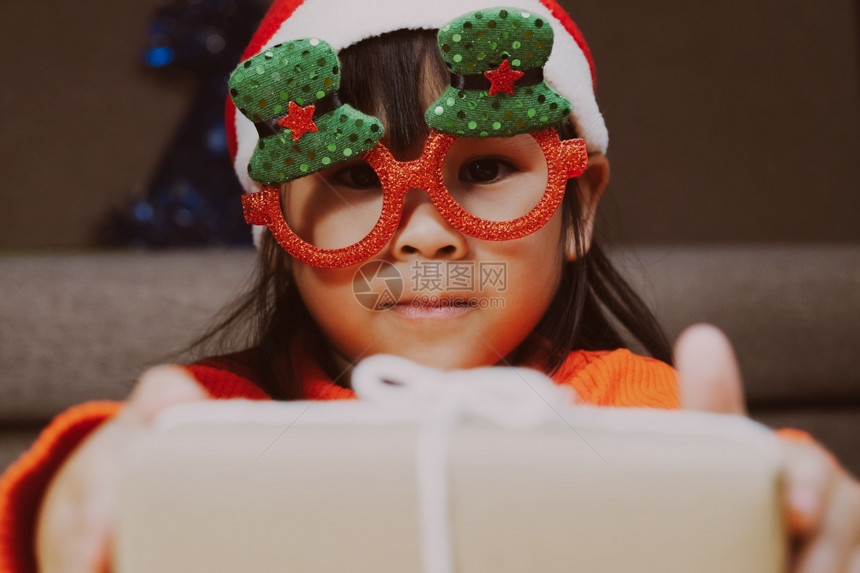 手势庆典快乐的小女孩戴着圣诞帽在家送礼物新年快乐圣诞红色的图片