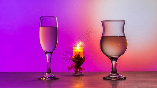 问候绿色红酒杯两白葡萄和桌上的蜡烛粉红色背景两杯白葡萄酒和桌上的蜡烛设计图片