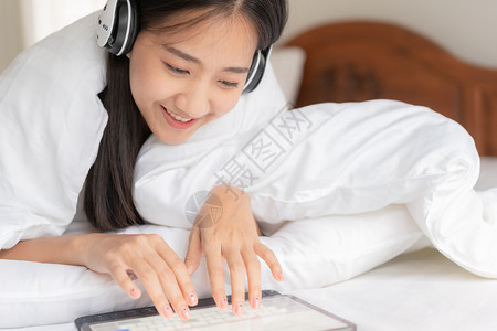 美丽的亚洲年轻女肖像正在休息床上监听音乐用平板电脑在家中娱乐用听音机与亚洲女孩一起睡觉年轻的现代随意漂亮的高清图片素材
