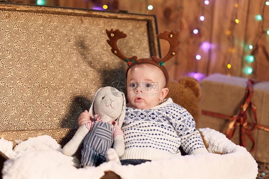 小男孩坐在一个手提箱里房间拿着玩具兔子装上圣诞饰品清白的克劳斯树图片