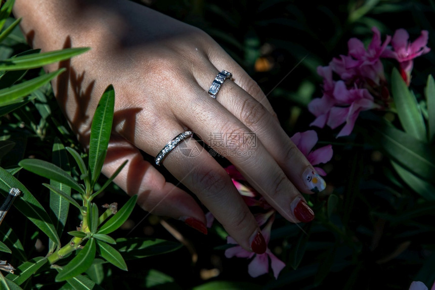 女手将银戒指戴在一位士的手指上红钉在粉色花朵上的红钉子优雅昂贵的一种图片