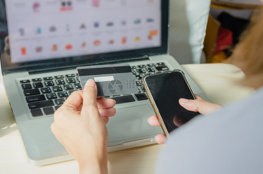 在线的持信用卡和智能电话的亚洲女手握信用卡和智能电话供家庭网上购物买电脑图片