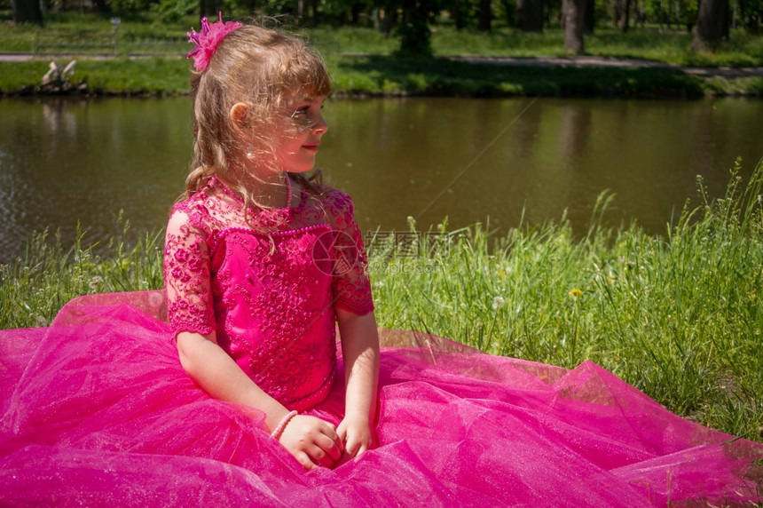可爱的夏天一个穿着豪华紫色礼服的小女孩坐在河边的草地上孩子图片