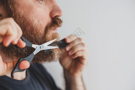 在隔离期间成年男子在家中用剪刀修剪胡子图片