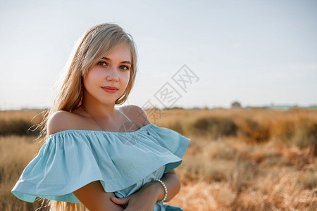烈日炎炎化妆品人们太阳身着浅蓝色礼服的美丽古巴年轻金发女孩站在田地上带着阳光遮的草地背景