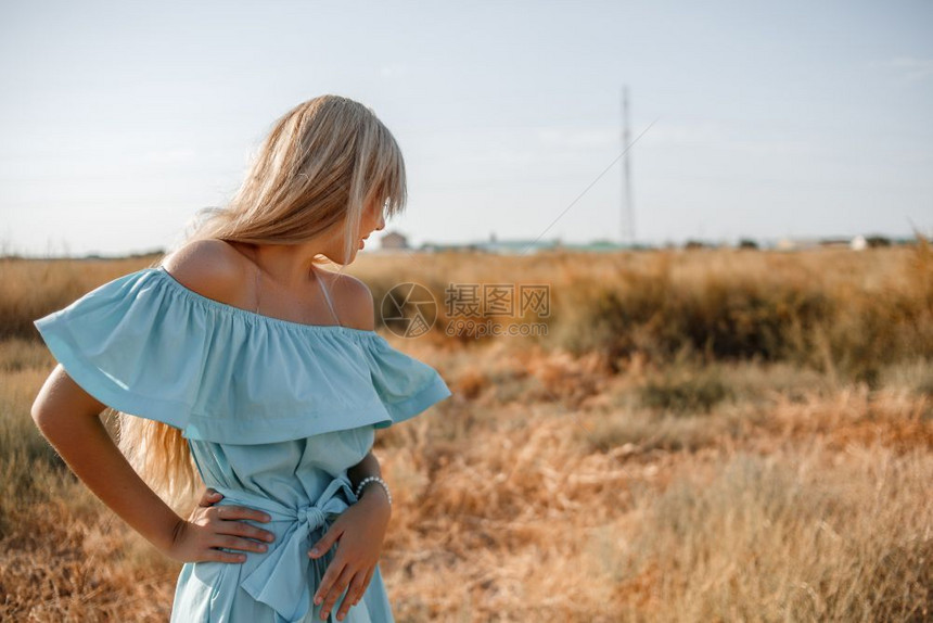 魅力场地蓝色的身着浅礼服的美丽古巴年轻金发女孩站在田地上带着阳光遮的草地图片