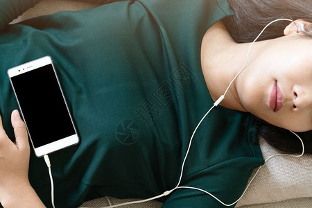 好播放器素材放松好的请享用在沙发上躺下用智能手机听音乐的美丽年轻女头部一眼背景