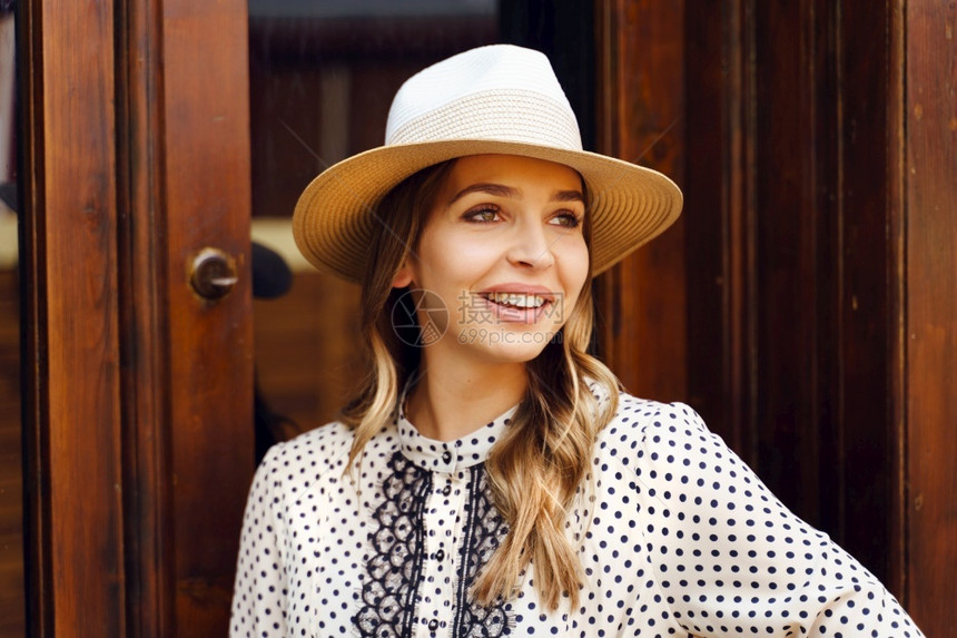 身着帽子和服装站在前门的年轻女子肖像时髦夏天微笑图片