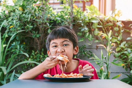 可爱的享受素食主义者穿着红衬衫的亚洲可爱男孩愉快地坐着吃披萨图片