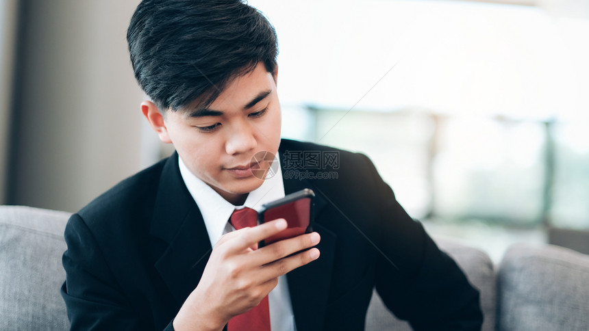 城市专业的青年商人使用移动电话应程序在办公室外与背景的摩天大楼通短信年轻商人持有智能手机从事商业工作的青年男子员工图片
