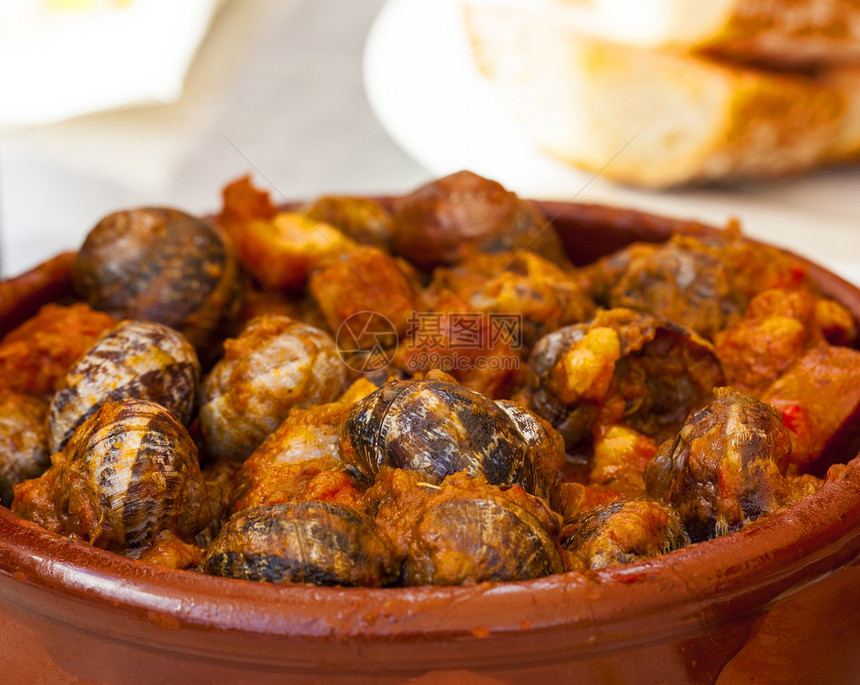 紧贴传统的西班牙土豆番茄酱加大蒜的煮蜗牛和黑铁锅中的辣椒色桌子美食图片