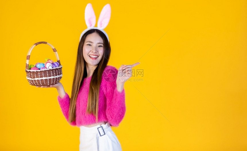 人们穿着兔子耳朵的亚洲快乐女青年手拿着一个篮子配彩色复活节鸡蛋在黄色空版间工作室背景上孤立无闻白种人复制图片