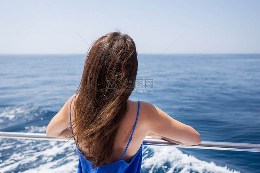 闲暇夏天年轻美丽的黑发女孩坐在游艇上背景是美丽的蓝色大海或年轻美丽的黑发女孩背坐在游艇上景是美丽的蓝色大海或人们图片