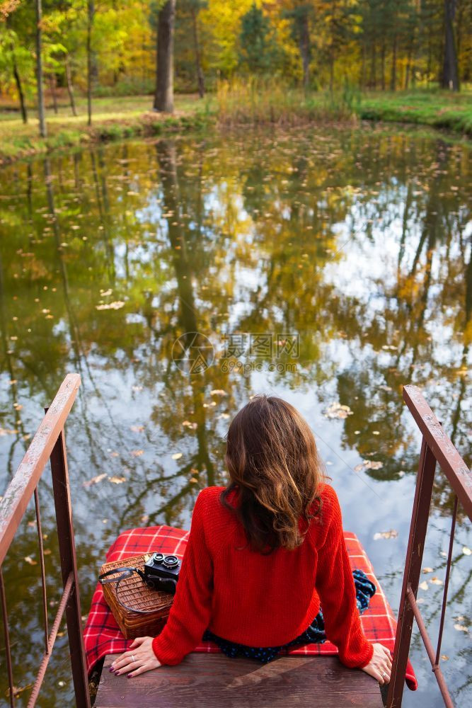 放松一个年轻女子在阳光明媚的日子里背坐在湖边的一座桥上美丽的秋天一个年轻女子在阳光明媚的日子里背坐在湖边的一座桥上美丽的秋天背部图片
