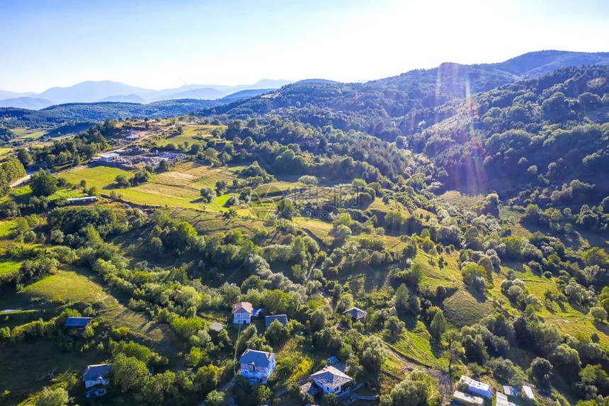 丘陵森林爬坡道无人驾驶飞机从空中观察美丽的山丘房屋和树木以及太阳耀斑的照片图片