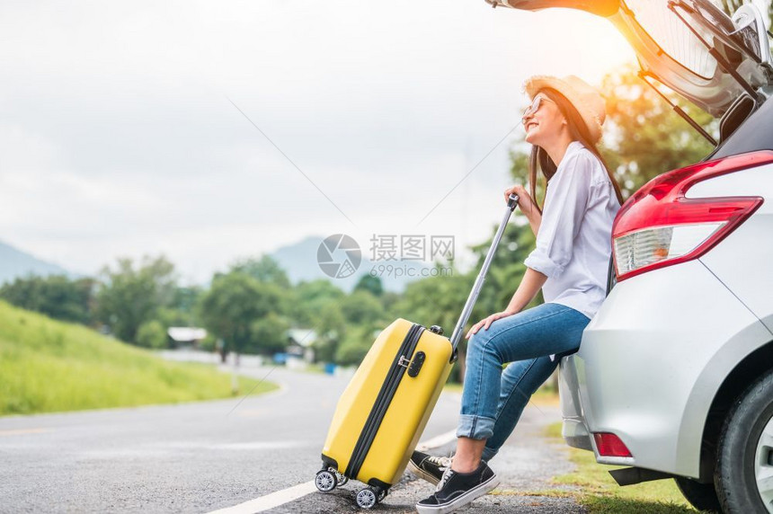 亚洲妇女在与黄行李同的路上度过周末女孩在汽车后背上放松有道路背景公旅行和假期概念人们的生活方式和交通路途快乐的开支趣图片