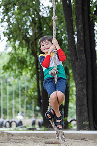 户外快乐一名男孩身着彩色鲜亮的衣服在操场上挂绳子玩并享受健康暑假活动愉快的期健康生方式的概念保持快乐的高清图片素材