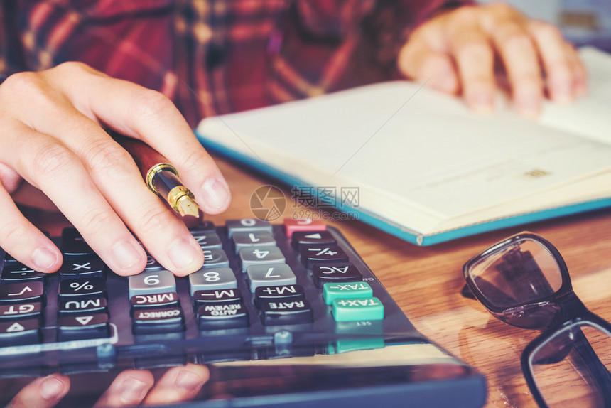 商家用手和计算器在家中做笔记利润花费文书工作图片