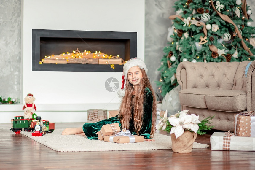 圣诞树下坐壁炉旁打开礼物的小女孩图片