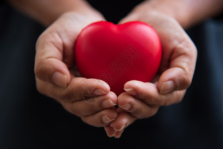 将红心贴紧双手作为心脏捐赠者给予红心作为爱的情人节日医疗通风器和心捐献者慈善悲与健康之手帮助自由生命捐赠药物血液妈背景