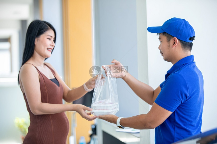 亚洲送货服务人员身穿蓝色制服有帽子用塑料袋处理食品箱在房子门前交给顾客在线购物和快车交货公司OnlinesessingandEx图片