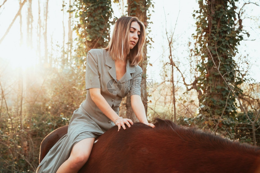 年轻的键户外美丽年轻女子骑着她的棕色马穿着衣服图片
