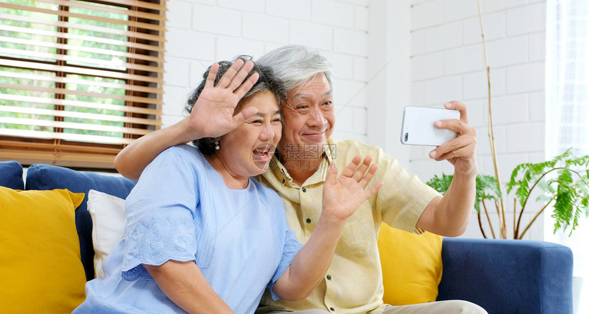 坐着健康年长的亚裔夫妇通过视频给家人打电话朋友在坐沙发上家客厅里时笑着开心地微老人和科技生活方式积极的老年人退休家庭图片