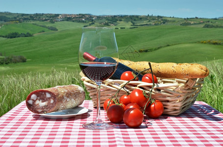 生活意大利语红葡萄酒面包和西红柿在彩布上与意大利的托斯卡纳风景对比吃图片