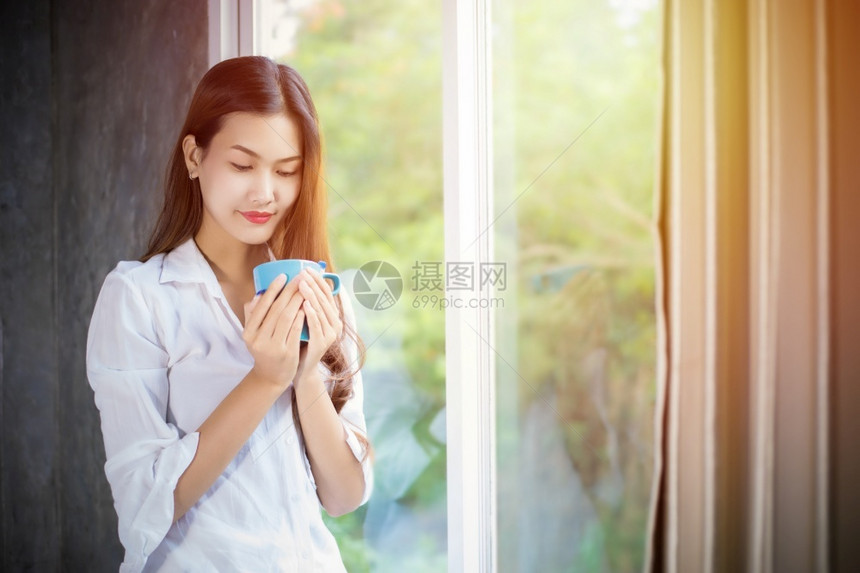 一名亚裔妇女站在咖啡杯上打开窗帘着当时她在家一天早上醒来后她站立在一旁女孩苏醒图片