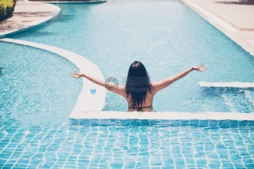 太阳休息水池女人穿比基尼和喝鸡尾酒在热暑假游泳池图片