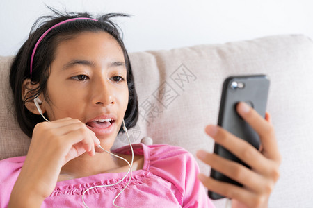 数字的亚洲女孩坐在家里客厅的沙发上在智能手机进行视频通话HappyAsia孩子脸上微笑用耳机聊天超越互联网生活方式和放松的概念尽愉快高清图片素材