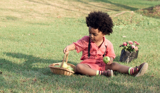 一个穿粉红衬衫的非洲小男孩在后院玩耍吃苹果家随意的挑战图片