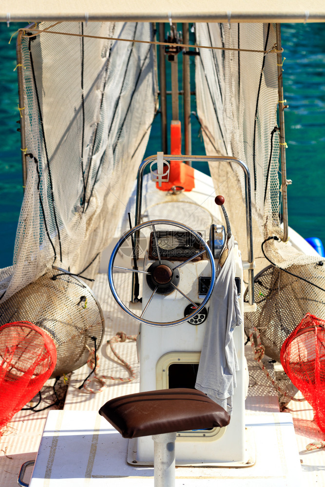 运输港口舰长桥方向轮渔网和船长在一艘小老渔船的操纵杆上驾驶T恤衫这艘小渔船在开阔海浪上游荡模糊地看到船长桥和驾驶一个挂着渔网的小图片
