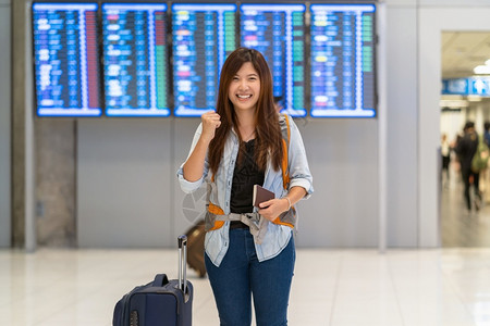 白种人在现代机场飞行信息屏幕上登机旅行和带有技术概念的交通方面携带行李和护照的亚洲旅行者在飞板上走过机牌在行信息屏幕上报到达电话快乐的高清图片素材