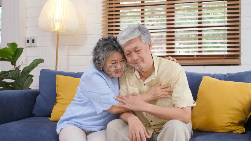 人们年长的亚裔夫妇在家中客厅坐沙发上时因情绪低落而互相安慰享受老年退休生活方式郁闷妻子图片